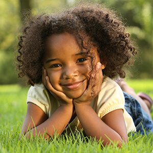 Young girl laying in grass after seeing pediatric dentist in Riverton