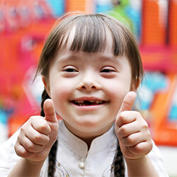 Young girl with special needs smiling and giving two thumbs up